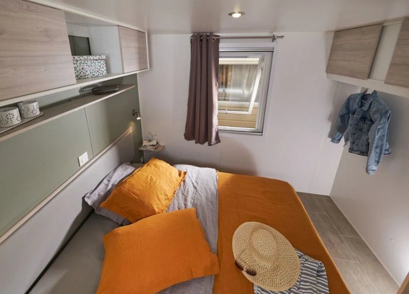 Ein kleines, modernes Schlafzimmer mit Bett, Vorhängen am Fenster, Nachttisch und einer aufgehängten Jacke.