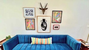 A blue sofa with a striped pillow, a cactus, and framed artwork on the wall. - Hacienda East - Central + Bright + Just Right (Austin)