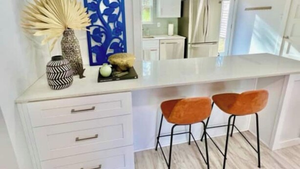 A modern kitchen with white cabinets, a stainless steel refrigerator, and two orange bar stools. - Hacienda East - Central + Bright + Just Right (Austin)