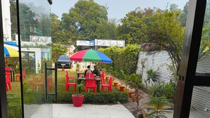 A glass door entrance to a hotel patio with outdoor seating, potted plants, and a clear view of the surrounding greenery. - Hotel A.D. Residency By Reverie (Agra)