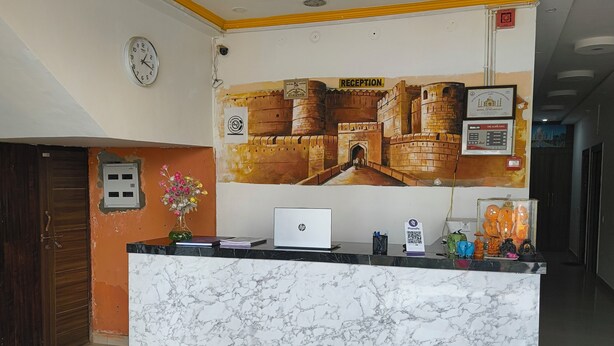 A reception desk with a marble top, a clock, and a mural of a castle. - Hotel A.D. Residency By Reverie (Agra)