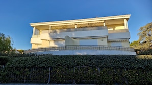 Un bâtiment moderne à deux étages, doté de balcons, d’un toit plat et entouré d’une haie.
