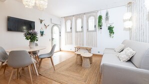 A modern living room with a grey sofa, a dining table with chairs, a TV mounted on the wall, and decorative elements like plants and wall art. - Garden Apartment La Bohémienne, Mandara Beach (Antibes)