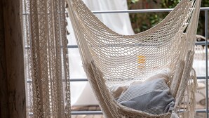 En hängmatta med en sittkudde, ett bord av rotting och en mönstrad gardin.