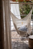 Un sillón hamaca con cojín, una mesa de mimbre y una cortina estampada.
