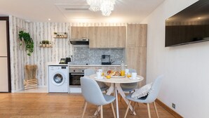 A modern kitchen with wooden cabinets, a washing machine, and a dining area with a round table and chairs. - Garden Apartment La Bohémienne, Mandara Beach (Antibes)