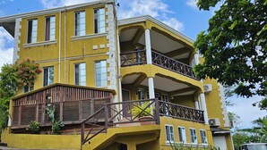 A multi-story yellow building with balconies, wooden shutters, and potted plants.