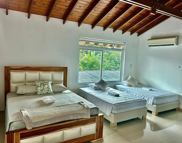A bedroom with two beds, a large window with a view of greenery, and a wooden ceiling. - Teka Hotel Villavicencio (Villavicencio)