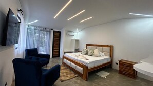 Um quarto moderno com uma cama, uma poltrona, uma televisão e uma escrivaninha.