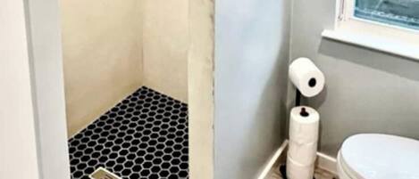 Un baño con ducha, inodoro y ventana.