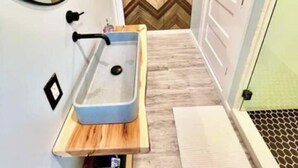 Une salle de bain moderne avec un lavabo intégré, un plancher en bois et un mur orné d’un motif en chevrons.
