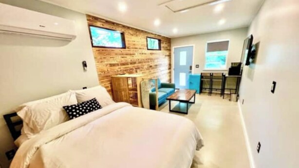 Une chambre d’hôtel moderne dotée d’un grand lit, d’un mur décoratif en bois, d’un petit coin salon et d’une kitchenette.