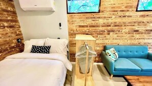 Une pièce avec un lit, un canapé bleu, un mur en bois et un téléviseur fixé au mur.