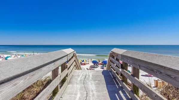 Une promenade en bois menant à une plage où se trouvent des parasols et des gens.