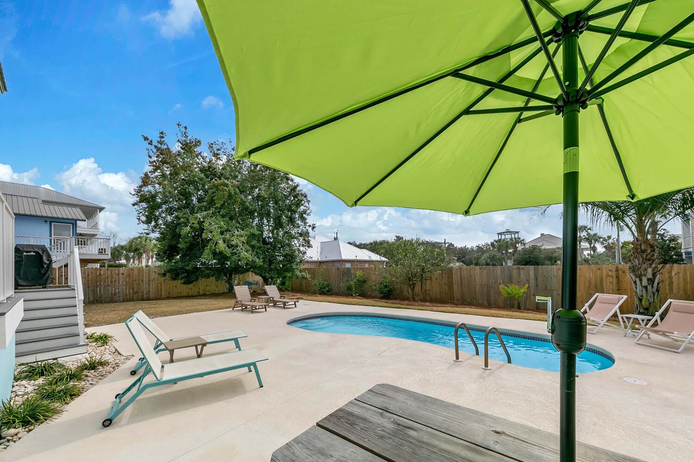 A backyard with a swimming pool, lounge chairs, and a green umbrella.