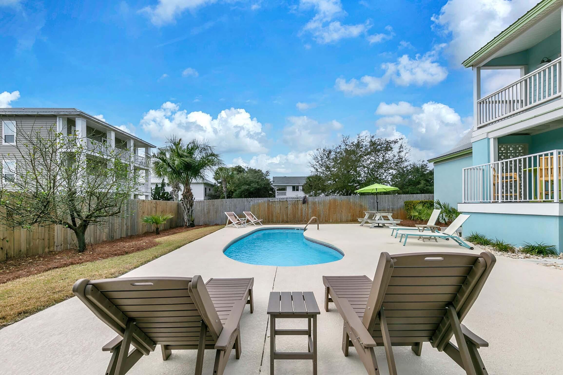 A backyard with a swimming pool, lounge chairs, and a wooden table.