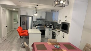 A modern kitchen with white cabinets, stainless steel appliances, and a dining area with a red tablecloth and two chairs. - PRIVATE, QUIET, CLEAN LEGAL SUITE FULLY FUNISHED. NEAR DOWNTOWN &TRAIN STATION (Edmonton)