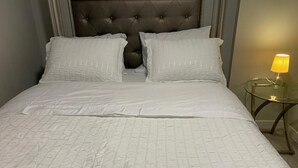 A neatly made bed with a quilted white bedspread and two pillows, a tufted headboard, and a bedside lamp on a small round table. - PRIVATE, QUIET, CLEAN LEGAL SUITE FULLY FUNISHED. NEAR DOWNTOWN &TRAIN STATION (Edmonton)