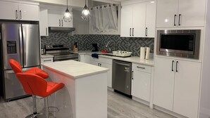 A modern kitchen with white cabinets, stainless steel appliances, a central island with a red chair, and pendant lighting. - PRIVATE, QUIET, CLEAN LEGAL SUITE FULLY FUNISHED. NEAR DOWNTOWN &TRAIN STATION (Edmonton)