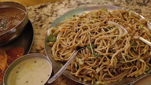 A plate of noodles with vegetables and a spoon, accompanied by a bowl of soup and a small dish of sauce. - Hotel Surya Inn  (Prayagraj)