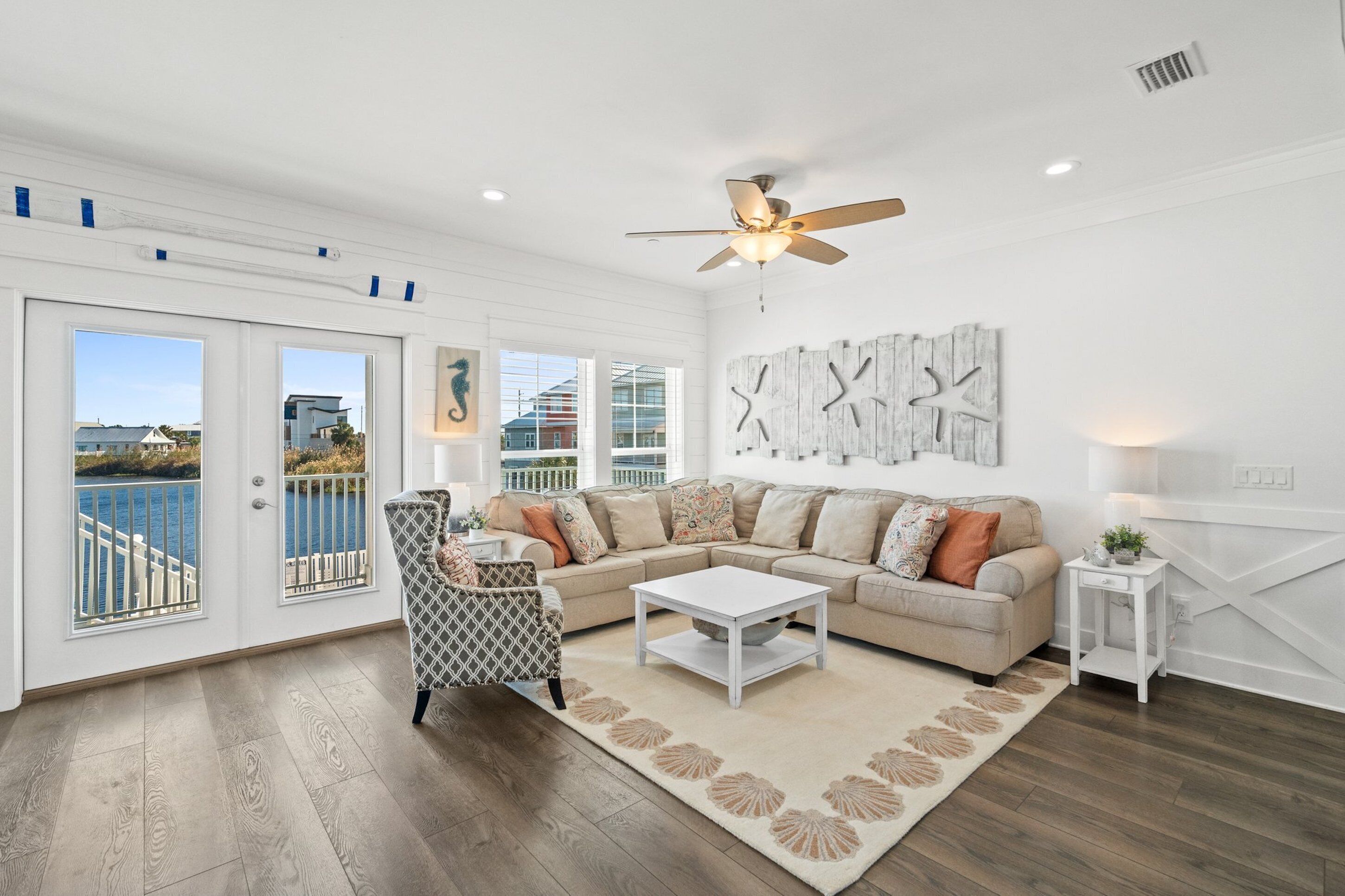 A spacious living room with a large window overlooking a balcony, a ceiling fan, and a modern sofa set.