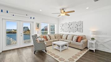 A spacious living room with a large window overlooking a balcony, a ceiling fan, and a modern sofa set.