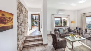A spacious living area with a stone wall, a staircase leading to an outdoor terrace, and a view of the city. - Apollon Dionysus Villa (Peyia)