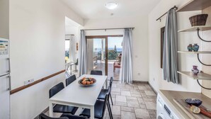 A compact kitchen with a dining area, a washing machine, and a view to the outside. - Apollon Dionysus Villa (Peyia)