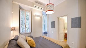 A bedroom with a bed, a window, a door, and a wall-mounted lamp. - The Garden of the Muse (Roma)