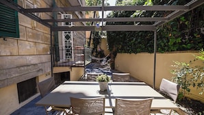 A covered outdoor patio with a table and chairs, a hammock, and a potted plant. - The Garden of the Muse (Roma)