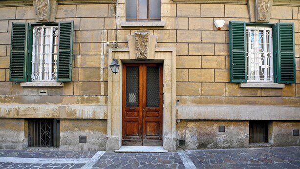 A building with a stone facade, a wooden double door with a glass panel, and green shutters on the windows. - The Garden of the Muse (Roma)