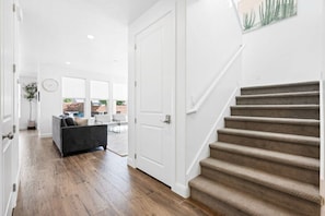A hallway with a staircase, wooden flooring, a grey sofa, and a white door. - 5 Bed Modern St George Oasis! (Washington)