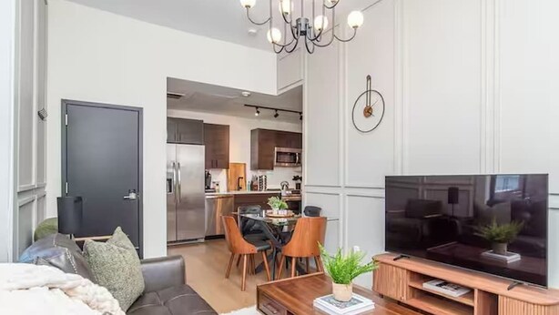 A modern living room with a sofa, coffee table, TV, and dining area. - LUXE Sun Drenched 2 Bd, Steps to Brown and Wayland (Providence)