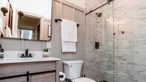 A modern bathroom with a marble shower wall, a toilet, and a sink with a mirror above it. - LUXE Sun Drenched 2 Bd, Steps to Brown and Wayland (Providence)
