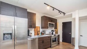 A modern kitchen with stainless steel appliances, wooden cabinets, and a microwave. - LUXE Sun Drenched 2 Bd, Steps to Brown and Wayland (Providence)