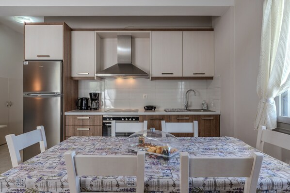 Une cuisine de taille réduite, avec des meubles blancs, un réfrigérateur en acier inoxydable et une table à manger recouverte d’une nappe à motifs floraux.