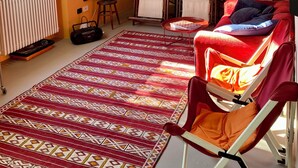 A cozy living room with a red sofa, a patterned rug, a bookshelf filled with books, and a large painting on the wall. - Villa in the Green in the hills in Lavagna - 3 Bedrooms, Garden and Private Parking (Lavagna)