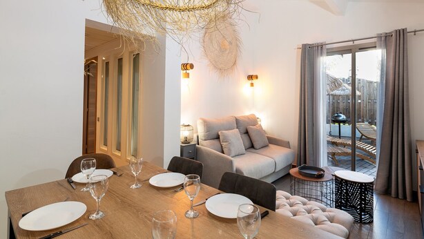 A modern dining area with a wooden table set for six, a sofa, and a balcony with a grill. - Private Garden La Cabane Bambou, Mandara Beach (Antibes)