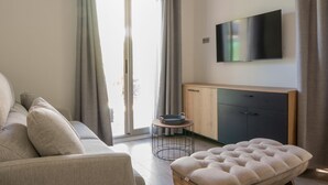 A modern living room with a sofa, a wooden ottoman, a TV, and a sliding glass door to the outside. - Private Garden La Cabane Bambou, Mandara Beach (Antibes)