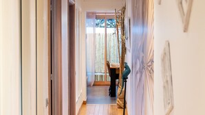 A hallway with wooden flooring, white walls, and a view into a dining area with a table and chairs. - Private Garden La Cabane Bambou, Mandara Beach (Antibes)