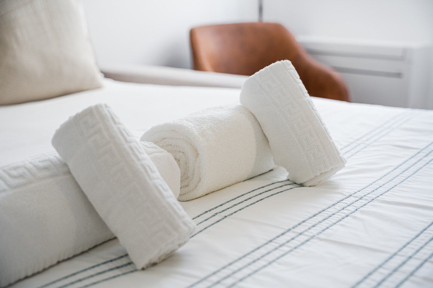 Una cama bien hecha con toallas blancas enrolladas y un edredón a rayas.