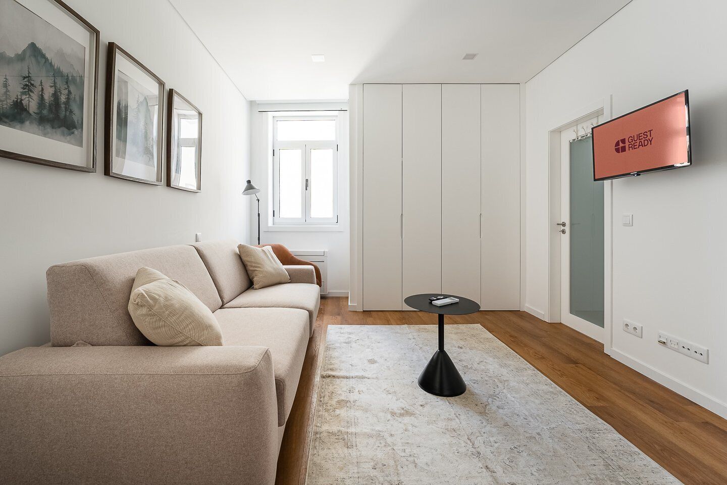 Una sala de estar moderna con un sofá, una mesita redonda y un televisor en la pared.