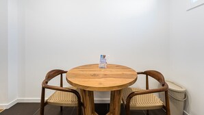A round wooden table with two wicker chairs, a calendar, and a trash bin in a room with white walls. - GuestReady - Inviting Hideaway in Matosinhos (Matosinhos)