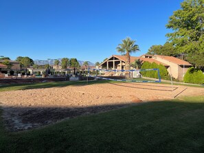 A sandy volleyball court with a net, surrounded by grass and trees, and a building with a red roof in the background. - Cozy 2-bedroom condo with WiFi, pools in charming St. George (St. George)