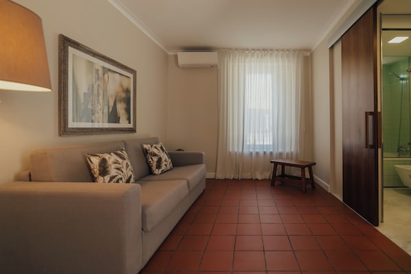 A living room with a sofa, a small table, a framed picture on the wall, and a sliding glass door leading to a bathroom.