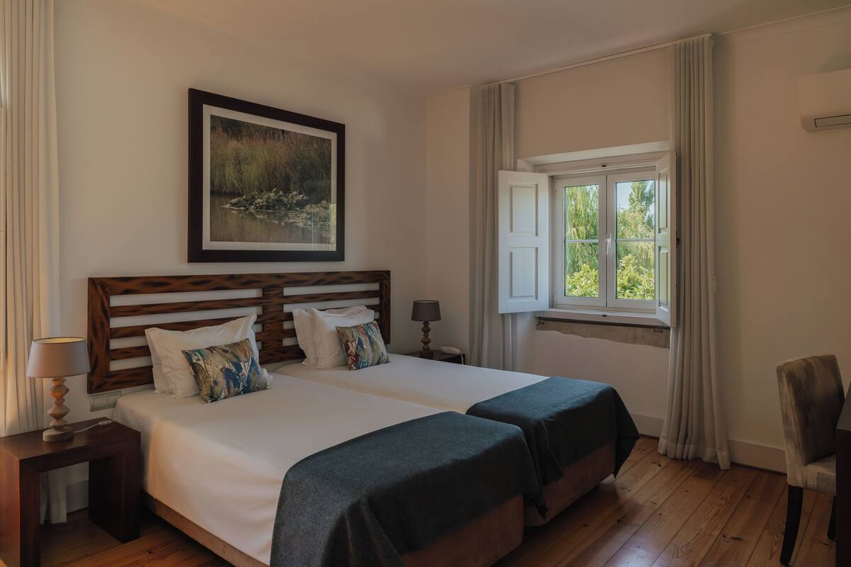 Un lit double avec une tête de lit en bois, deux tables de chevet avec des lampes, une fenêtre avec des rideaux et une chaise.