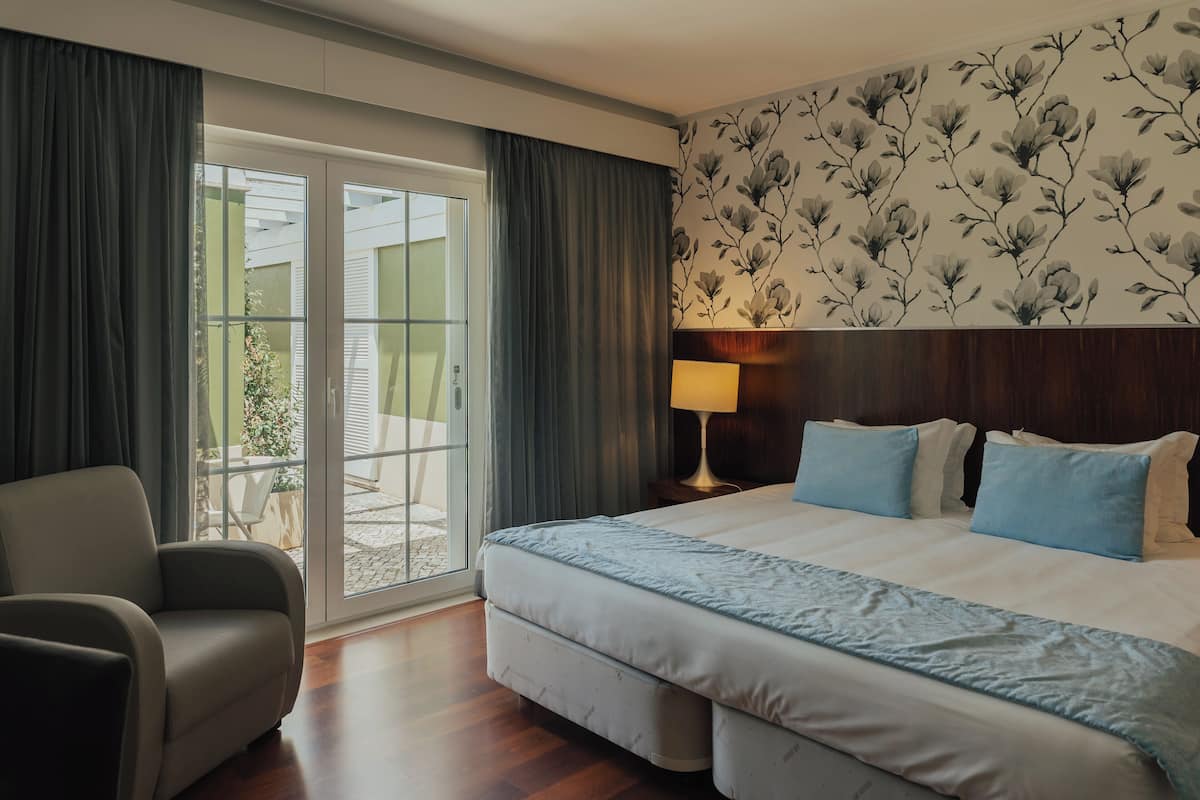 Une chambre d’hôtel avec un lit, une chaise, une table de chevet avec une lampe et une vue sur l’extérieur, accessible par une porte coulissante.