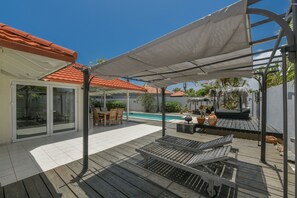 A covered outdoor area with a pool, wooden deck, and seating.