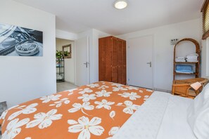 A bedroom with a bed, a wardrobe, a wicker chair, and a wall-mounted shelf with towels.