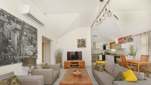 A living room with a sofa, a coffee table, a TV, and a dining area with chairs and a table.